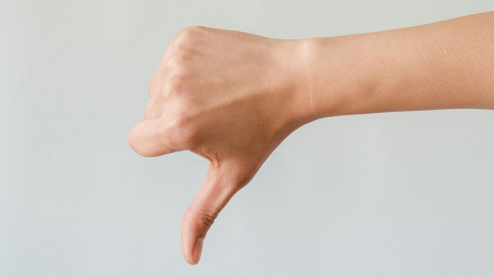 A close-up of a hand showing a thumbs down gesture against a light blue backdrop.